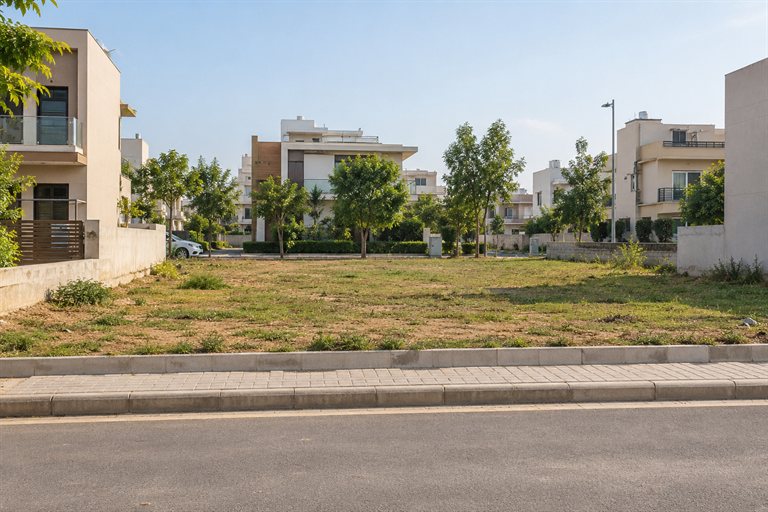 Illustrative vacant residential plot beside a paved road and neighbouring houses